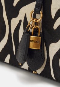 Bolso de mano con estampado de cebra en blanco y negro, con herrajes dorados, que presenta un candado y acentos texturizados en negro en las correas.