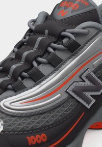 Gros plan de la baskets New Balance 1000 grises et noires avec des accents orange et un design unique de lacets bouclés.