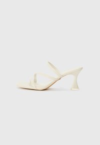 Beige high-heeled sandals with a square toe, featuring three slender straps and a sculptural, transparent heel. Smooth texture.