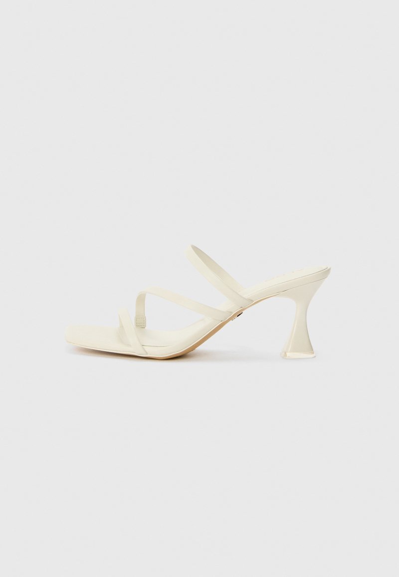 Beige high-heeled sandals with a square toe, featuring three slender straps and a sculptural, transparent heel. Smooth texture.