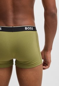 Grüne Baumwoll-Boxershorts mit einem schwarzen elastischen Bund, auf dem "BOSS" in weißen Buchstaben steht. Glatte Textur, enganliegendes Design, Oberschenkel-lange.