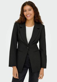 Must värviga ülikondjakk, millel on ühekohaline kinnitis, krae, esikotid ja pikad varrukad, kantud valge pluusi kohal.