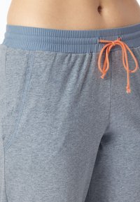 Pantalones deportivos de color gris claro con cintura acanalada y cuerda de ajuste naranja; cuentan con bolsillos laterales y una tela suave y texturizada.