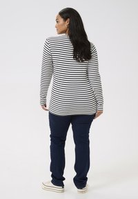 Haut à manches longues rayé en noir et blanc, associé à un jean bleu foncé et des baskets blanches. Tissu lisse, coupe décontractée, design casual.