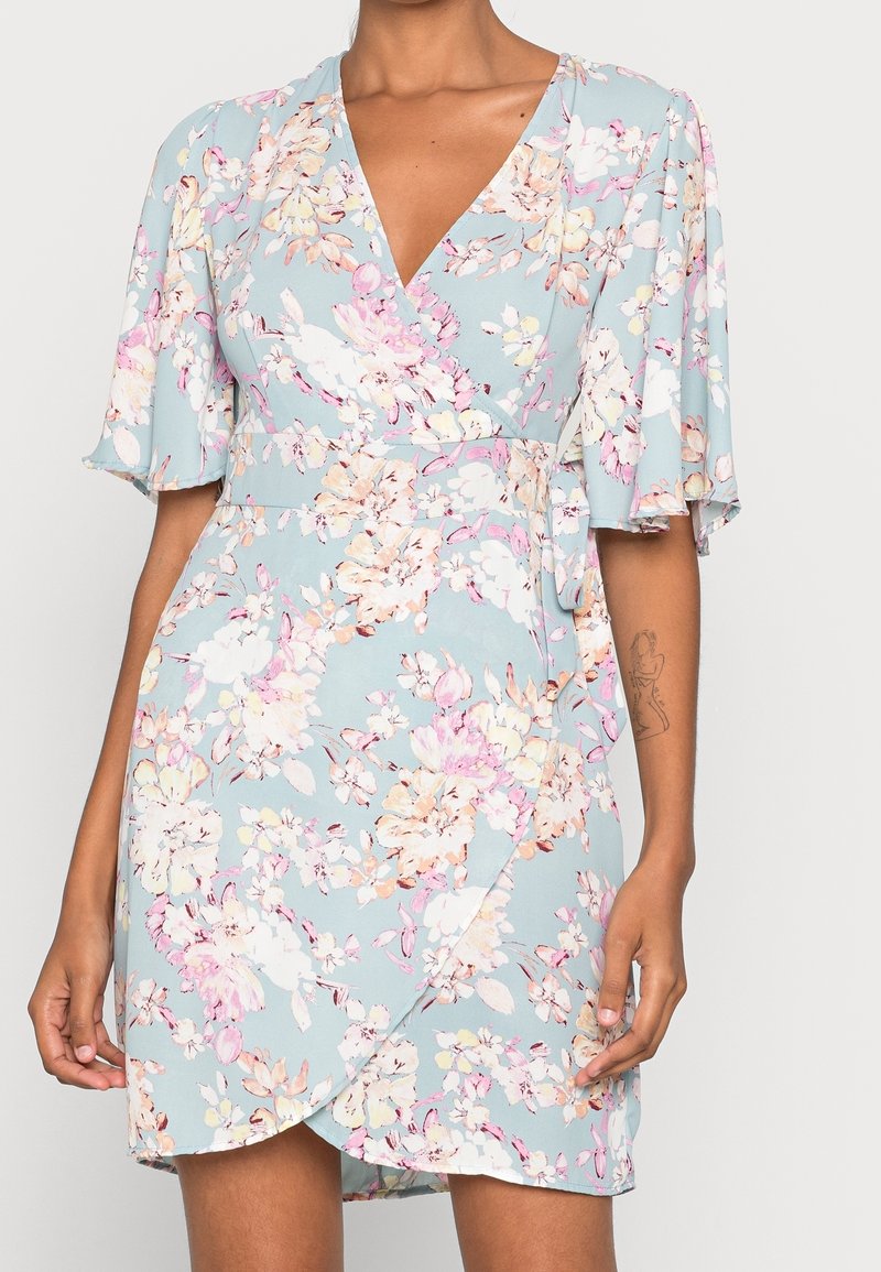 Květinové zavinovací šaty v světle modré barvě s krátkými volánovými rukávy, růžovými a bílými květinovými vzory a pevně utaženým páskem.