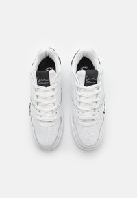 Hvide sneakers med perforeret læderoverdel, snørebåndsdesign, sort branding på tunge og glat gummisål. Minimalistisk æstetik.