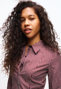 Vinröd skjorta med vita vertikala ränder, med krage och mjuk textur, framhävd av rundade knappar.