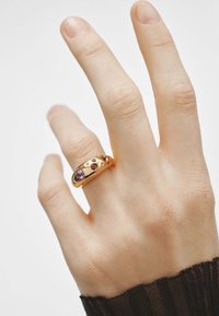 Anillo de oro con piedras preciosas moradas de varios tamaños, con un diseño suave y redondeado y sutiles acentos elevados en una mano.