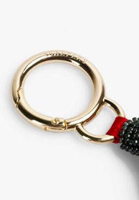 Llavero de metal con tono dorado y acabado texturizado. Cuenta con un broche lateral y una correa tejida roja con detalles de cuentas negras.