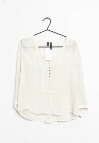 Camicia bianca con pois testurizzati, scollatura a V e placket a tre bottoni. Maniche lunghe con polsini leggermente arrotolati. Tessuto leggero e trasparente.