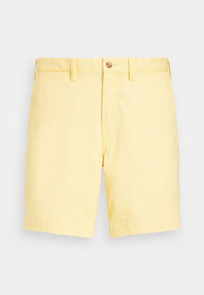 Calções amarelo claro feitos de algodão com fecho de botão, apresentando frente lisa, bolsos laterais e um corte reto acima do joelho.