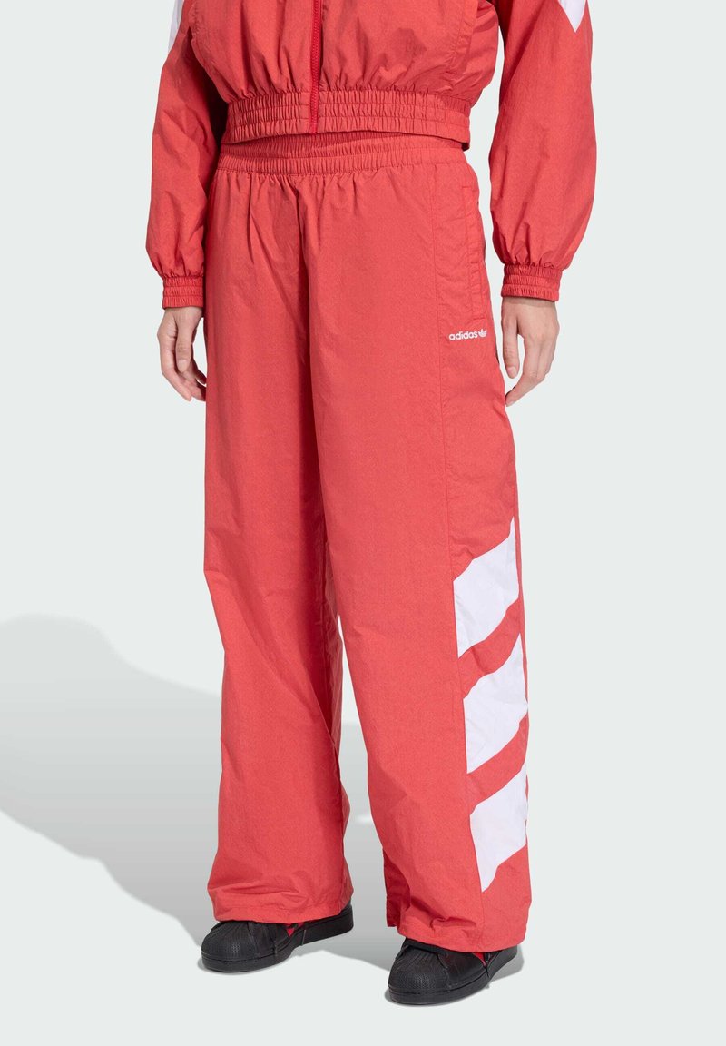 Červené atletické nohavice s bielymi diagonálnymi pruhmi po stranách, vyrobené z ľahkého, štruktúrovaného materiálu, s elastickým pásom.