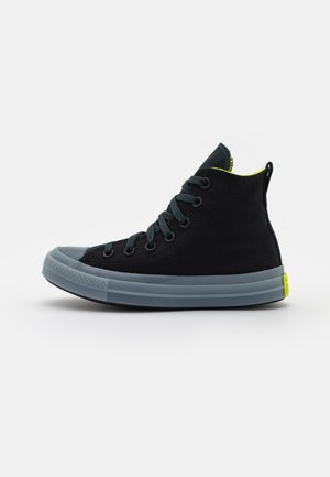 Black high-top sneaker with a textured fabric upper, gray rubber sole, dark laces, and a bright yellow accent at the heel.