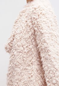 Dunig, texturerad cardigan i ljusrosa med en lös, bekväm passform. Har en mjuk, ludden yta och design med sänkt axel.