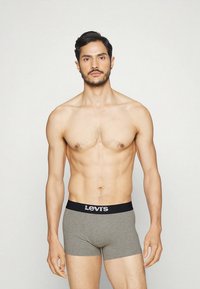 Homme torse nu aux cheveux courts et foncés portant un boxer gris Levi's, debout devant un fond clair uni, faisant face à l'avant.