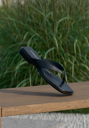 Juodas flip-flop tipo batai su plokščia padu ir plonomis dirželiais. Pagamintas iš lygaus kaučiuko, pasižymintis minimalistiniu dizainu. Paprastas prekės ženklinimas ant pado.