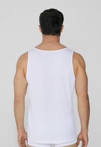 Camiseta sin mangas de algodón blanca con un corte holgado, tirantes anchos y una textura suave, llevada por una figura masculina de espaldas al espectador.