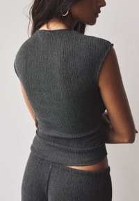 Crop top gris à côtes avec des manches courtes, présentant un tissu texturé. Le design comprend une silhouette ajustée et un détail subtil au niveau de la taille.