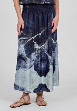 Femme portant une jupe longue fleurie bleu marine et blanche avec une taille élastique et des sandales plates à brides beige.