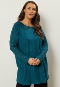 Maglia a maniche lunghe teal con scollatura ampia, caratterizzata da accenti in grommet argentati lungo le maniche e un tessuto morbido e testurizzato.