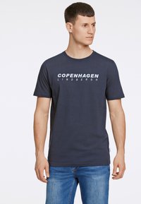 Kaulus sininen lyhythihainen t-paita, joka on valmistettu puuvillasta. Edessä valkoisella tekstillä lukee "COPENHAGEN LINDHBERGH". Klassinen istuvuus.