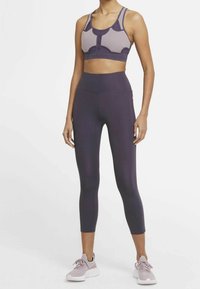 Ensemble de brassière de sport et de leggings en violet profond. La brassière présente des panneaux en maille ; les leggings sont ajustés avec une texture lisse. Complété par des chaussures violettes claires.