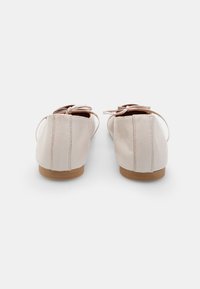 Jasnoróżowe baleriny z zaokrąglonym noskiem, wykonane z materiału skórzanego, z delikatnymi kokardkami i brązową gumową podeszwą. Pokazano widok z tyłu.