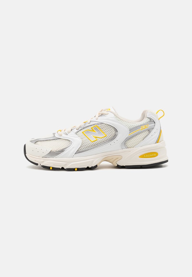 Baskets de sport blanches et grises avec des accents jaunes, des panneaux en mesh, le logo « N » et une semelle amortie, présentées de profil sur un fond neutre.