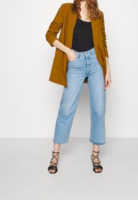 Hořčicový blazer, černý top na ramínka, světle modré zkrácené džíny a černé sandály na páscích. Blazer má klopu a volný střih.