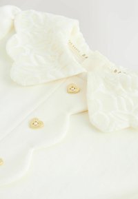 Witte blouse met een geannetste kantkleur, golfranden en drie gouden hartvormige knopen met bloemmotieven aan de voorkant.