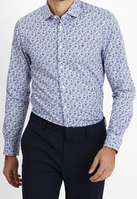Button-up shirt featuring a white base with a blue floral pattern. Made from lightweight fabric, it has a classic collar and long sleeves.