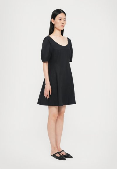 Black puff-sleeve dress with a square neckline, flared silhouette, and smooth texture. Paired with black flat shoes featuring straps.