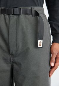 Sive hlače s teksturiranim materijalom, podesivim remenom i oznakom s logotipom "The North Face" na pojasu.
