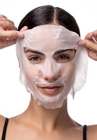 Hydratisierende Tuchmaske aus dünnem, weißen Stoff, die das Gesicht bedeckt und so gestaltet ist, dass sie sich an die Gesichtsformen anpasst, von Händen in der Nähe des Haaransatzes gehalten.