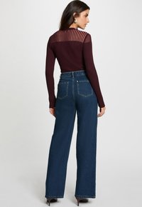 Haut bordeaux à manches longues côtelé avec un dos transparent rayé, associé à un jean large taille haute bleu foncé et des chaussures à talons.