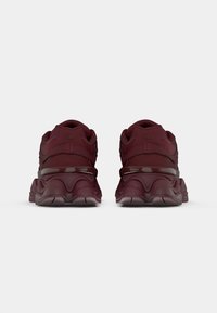 Bordeaux hardloopschoenen met een gestructureerde bovenkant, dikke zool met golven en glanzende enkelsteunen. De achterzijde toont logo-details.