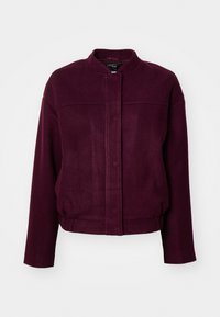 Veste en polaire bordeaux avec un col rond, des manches longues et une taille élastique. Présente une fermeture à l'avant et des coutures décoratives.