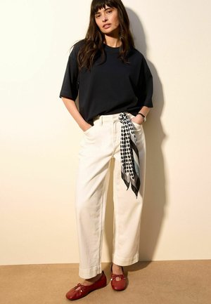 Woman wearing black oversized T-shirt, white high-waist wide-leg pants with black-and-white polka dot scarf, and red ballet flats.