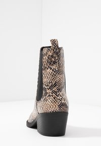 Bottine hauteur cheville avec un motif de cuir serpent marron et noir, panneau élastique latéral noir, tirette à l'arrière et talon large noir.