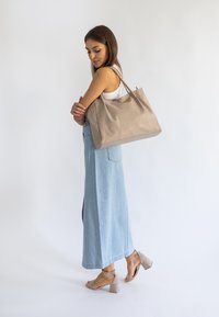 Beżowa skórzana torba na ramię o miękkiej fakturze i dwóch uchwytach, w połączeniu z jasnoniebieską spódnicą dżinsową i jasnymi sandałami na słupku.