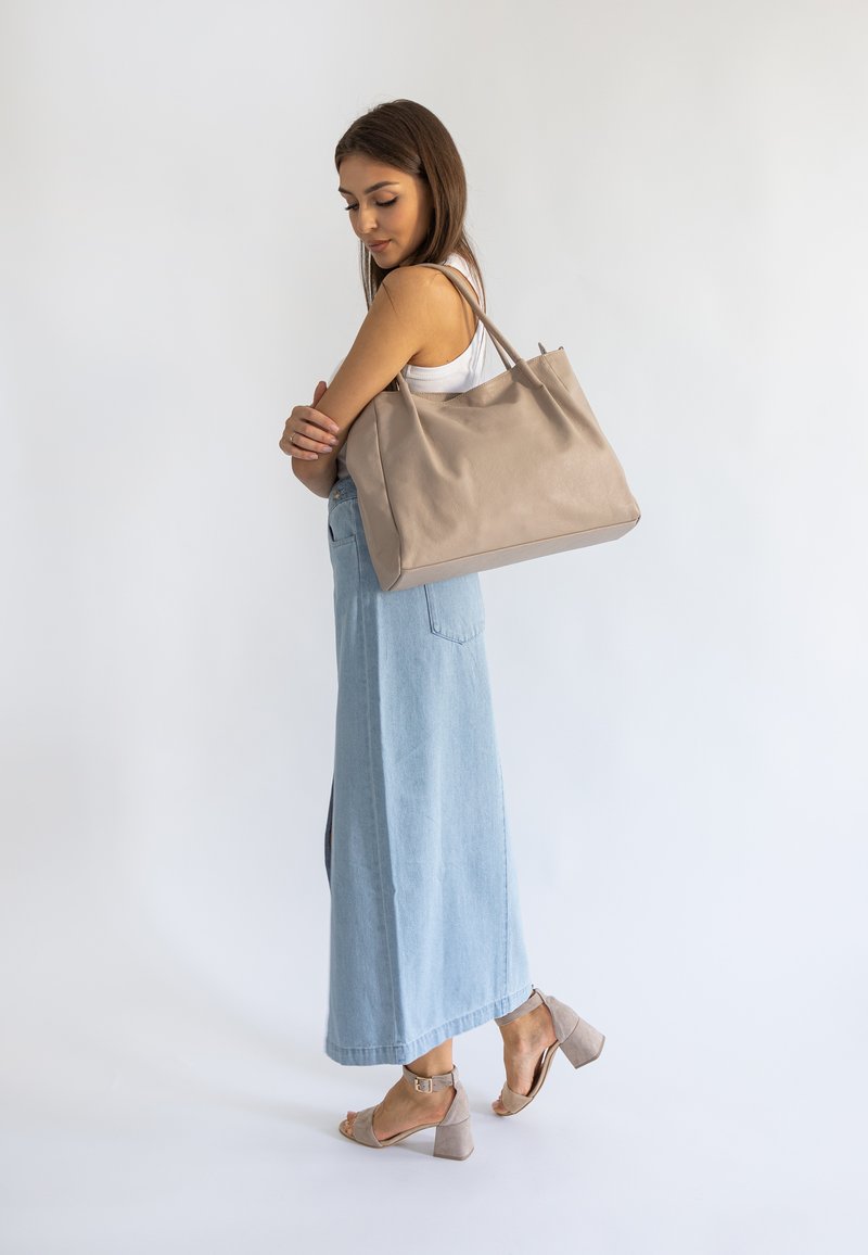 Beżowa skórzana torba na ramię o miękkiej fakturze i dwóch uchwytach, w połączeniu z jasnoniebieską spódnicą dżinsową i jasnymi sandałami na słupku.