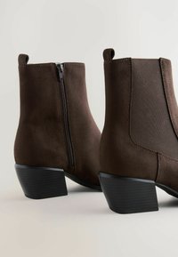 Brown suede ankle boots with a side zipper, elastic accents, and a low block heel. Smooth texture with a matte finish.
