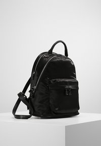 Musta nailonireppu pyöreällä muotoilulla, kaksoissyötöillä, etutaskulla, säädettävillä olkahihnoilla ja yläkahvalla. Sujuva pinta.