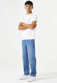 Camiseta blanca de manga corta, jeans rectos azules y zapatillas blancas. El conjunto presenta un ajuste casual y un diseño simple sin patrones.