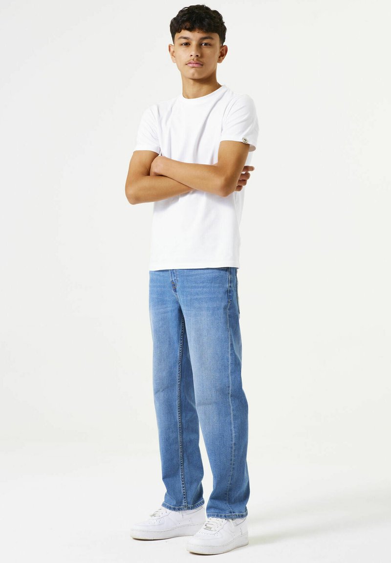 Camiseta blanca de manga corta, jeans rectos azules y zapatillas blancas. El conjunto presenta un ajuste casual y un diseño simple sin patrones.