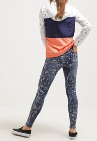 Farveblokket vindjakke med hvide, marineblå og koralfarvede sektioner; parret med mønstrede denim leggings; sorte slip-on sko.