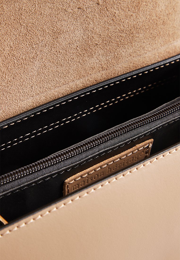 Wnętrze beżowej skórzanej torebki, z czarną kieszenią na zamek, zamszowym wykończeniem i oznaczonym taniej skórzanym metką. Widoczne kontrastowe szwy.