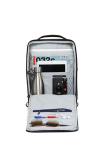 Grauer Rucksack, der geöffnet ist und eine silberne Wasserflasche, ein Tablet, eine Kamera, eine Sonnenbrille, einen Stift und Kopfhörer zeigt, die alle in Fächern organisiert sind.