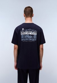 Navy blue cotton t-shirt featuring a graphic print of mountains and trees on the back, with "NAPAPIJRI" text above. Short sleeves, relaxed fit.