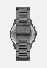 Mustmust kell, millel on linkidega rihm ja millel on graveeritud logo lukul. Ümmargune korpus, millel on nähtavad seadmed ja lihtne valge kellanägu.